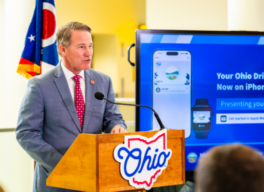 Senator Jon Husted speaking at a podium in front of the Ohio flag
